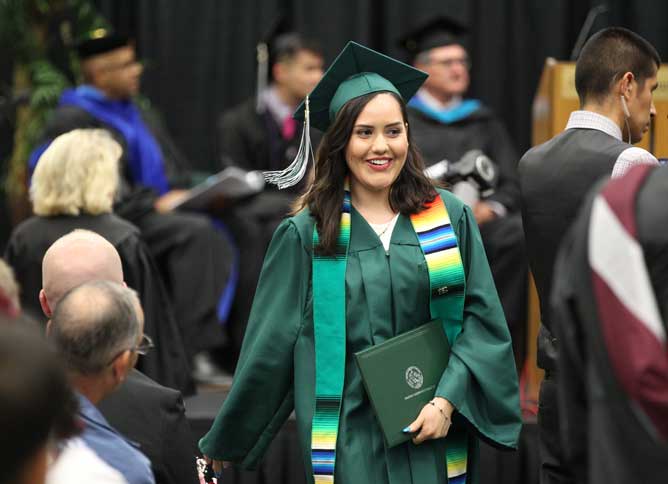 Student wearing Latinx stole carries diploma in crowd.