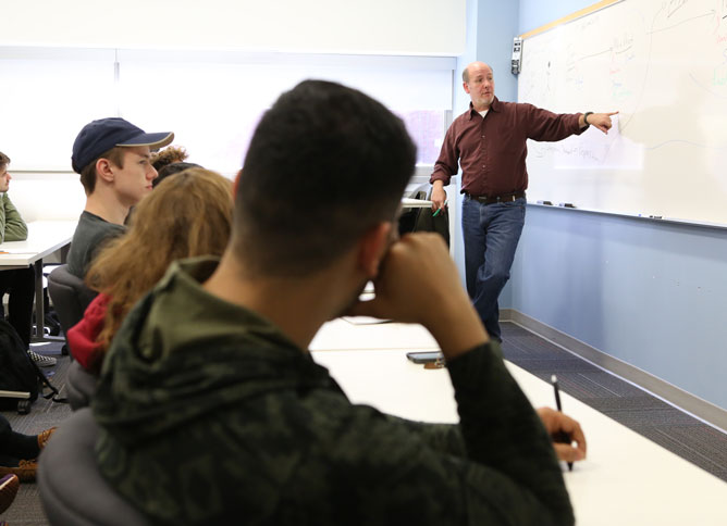 Professor pointing to board as class listens.