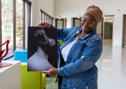 Oakton student holds up original artwork, a portrait with the head exploding.