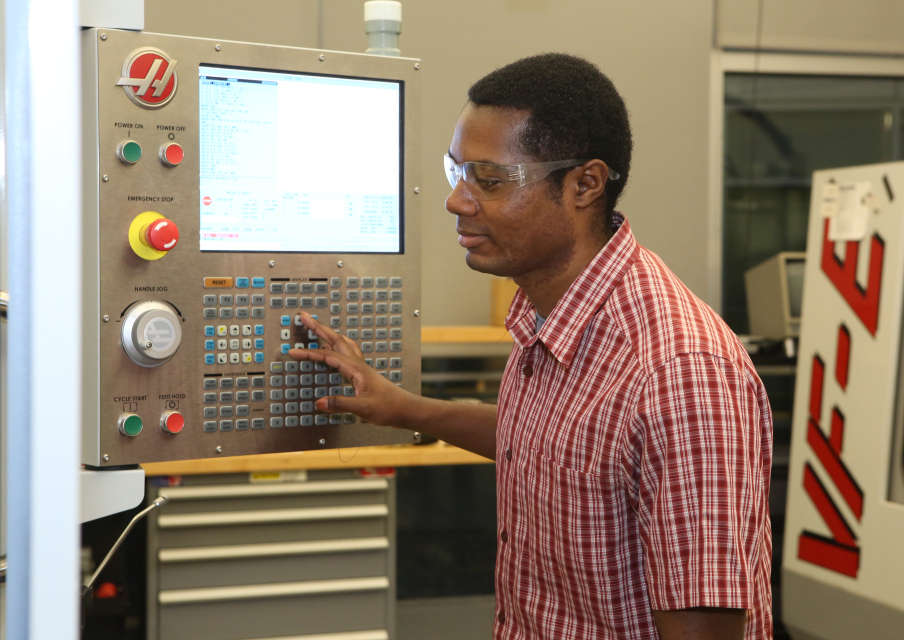 A photo of an African-American man operating a piece of mechanical equipment in a manufacturing setting.